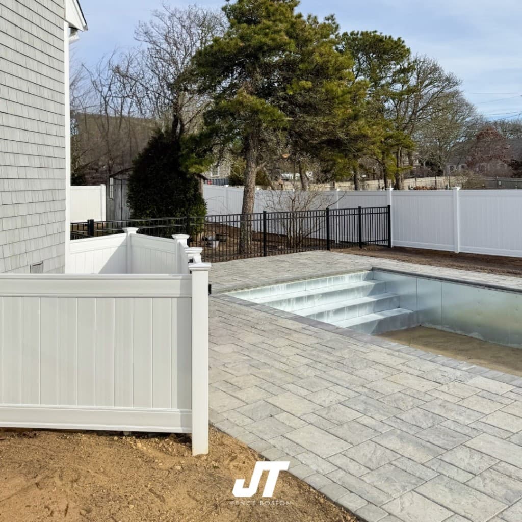 Stone paver pool deck under construction with white vinyl privacy fence and black metal pool barrier — JT Fence Inc.