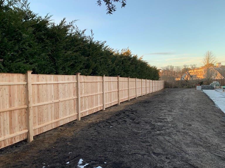Wood privacy fence installation by JT Fence Inc. — natural cedar-toned boards along a Massachusetts residential property